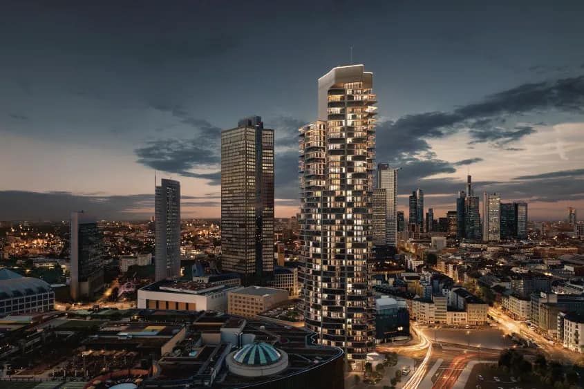 Visualisierung: Der beleuchtete Wohnturm in der Abenddämmerung vor der Frankfurter Skyline, im Vordergrund die Dachlandschaft eines Einkaufszentrums.